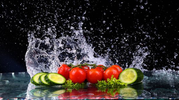 Studio shot with freeze motion of cherry tomatoes and slices of cucumber in water splash on black background - Photo, Image