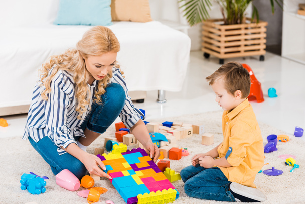 focused mother and little son playing with toys together on floor at home - Φωτογραφία, εικόνα