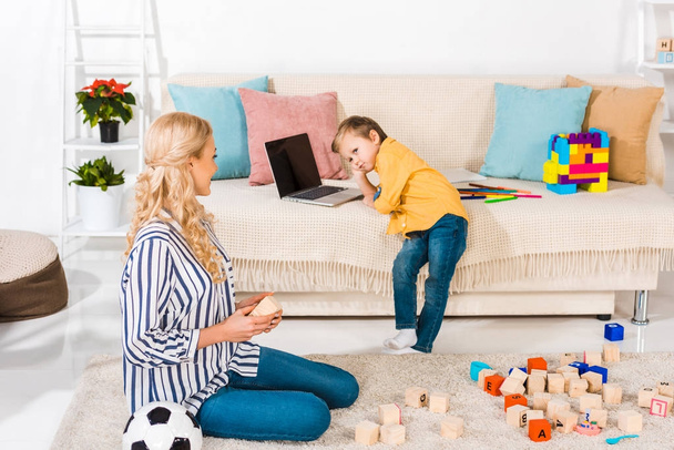 little boy using laptop on sofa while mother sitting on floor at home - Foto, Bild