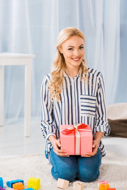 portrait of happy woman with wrapped gift in hands looking at camera at home - Фото, изображение