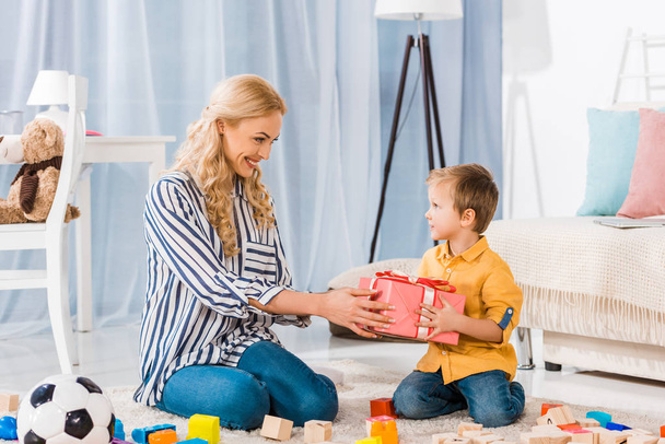 Lächelnde Mutter überreicht Geschenk an kleinen Sohn zu Hause - Foto, Bild