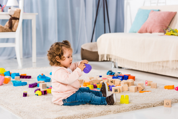 boční pohled na rozkošné dítě hrát s plastovými bloky na podlaze  - Fotografie, Obrázek