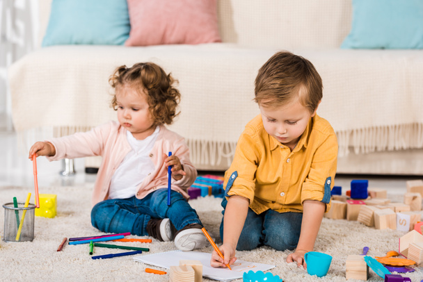 adorables hermanos jugando en un piso con lápices de colores
 - Foto, imagen