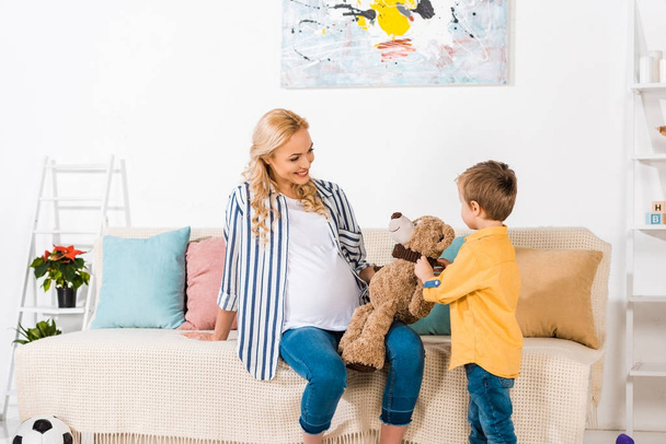 smiling pregnant mother presenting son teddy bear - Foto, afbeelding
