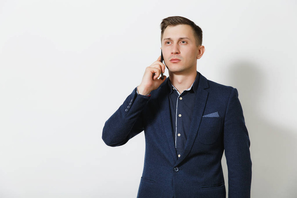 Pohledný kavkazské mladých obchodní muž v modrých Klasický oblek, košile mluvit na mobilním telefonu, vedení příjemnou konverzaci, izolované na bílém pozadí. Manažer, dělník. Kopírovat prostor pro reklamu - Fotografie, Obrázek