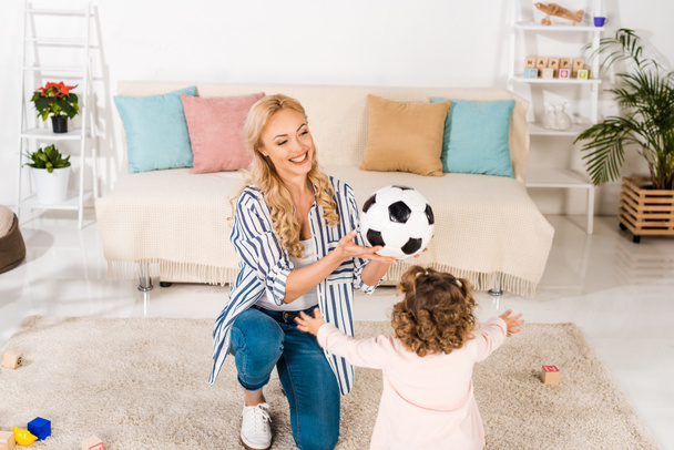 high angle view of happy mother and cute little daughter playing with soccer ball at home - Fotoğraf, Görsel