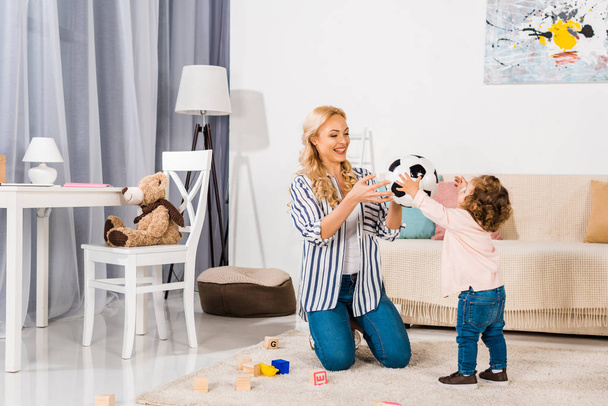 feliz madre y linda hijita jugando con pelota de fútbol en casa
 - Foto, Imagen