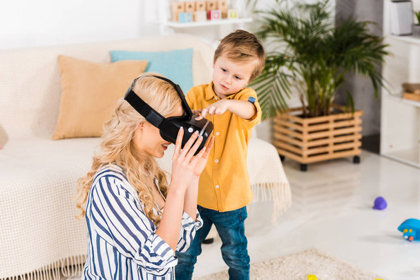 adorable little boy helping mother using virtual reality headset at home - 写真・画像