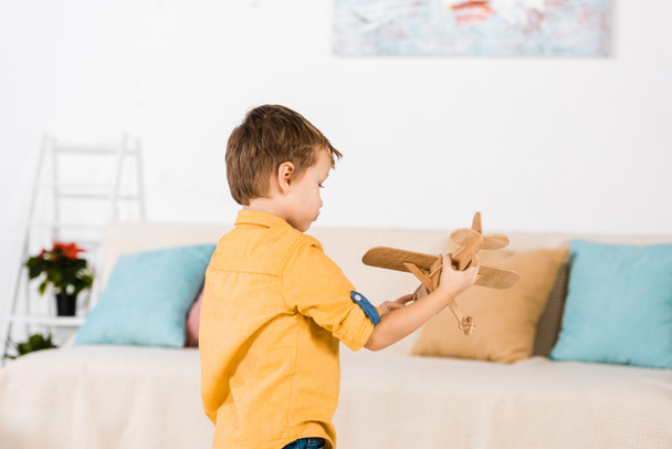 kleine schattige kleine jongen spelen met houten speelgoed vliegtuig thuis - Foto, afbeelding