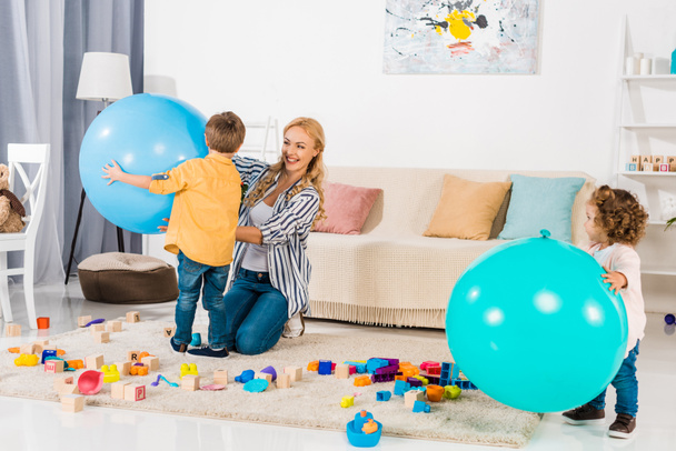 onnellinen äiti ja lapset leikkivät kuntopalloilla ja värikkäillä lohkoilla kotona
 - Valokuva, kuva