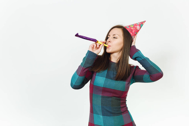 Красивая кавказская веселье молодая счастливая женщина в клетчатом платье и шляпа день рождения с застенчивой очаровательной улыбкой, играя трубки, празднуя и наслаждаясь праздником на белом фоне изолированы для рекламы
. - Фото, изображение