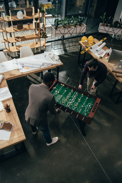 высокий угол зрения мультиэтнических архитекторов, играющих в настольный футбол в офисе
 - Фото, изображение