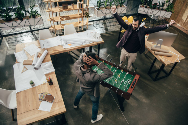 high angle view of young architects playing table football in office - Photo, Image