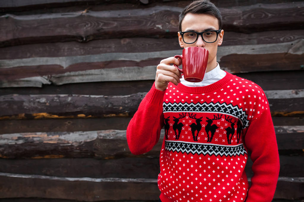Portrait of a boy in a Christmas sweater drinking coffee, on a background of wooden wall.  - Fotó, kép