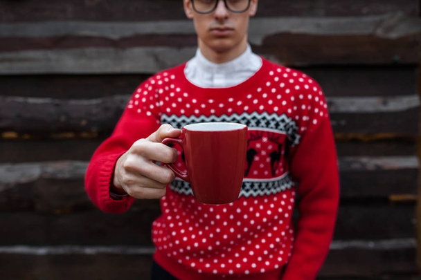 Portrait of a boy in a Christmas sweater drinking coffee, on a background of wooden wall.  - Foto, Imagen