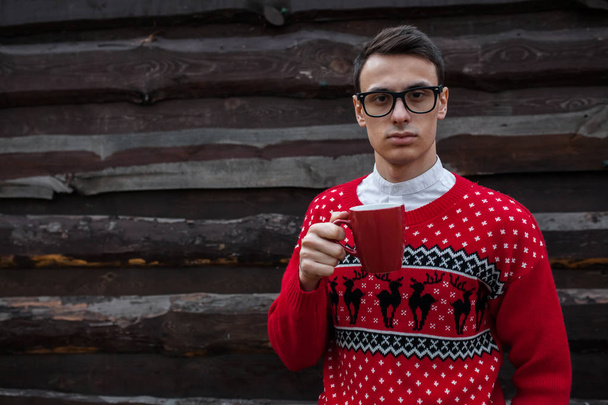 Portrait of a boy in a Christmas sweater drinking coffee, on a background of wooden wall.  - Foto, Bild