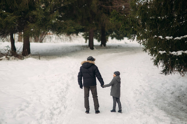 Glücklicher Vater mit Sohn spaziert bei verschneitem Winterwetter durch den Park - Foto, Bild