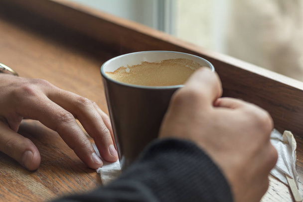 Xícara de café nas mãos de um homem deitado em uma mesa no café
 - Foto, Imagem