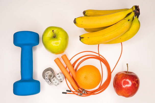 healthy eating concept. Dumbbell, rope, bananas, orange, measuring tape waist, oranges, red apple, green apple, on a white table. healthy lifestyle. sport. Fitness diet - Foto, Imagem
