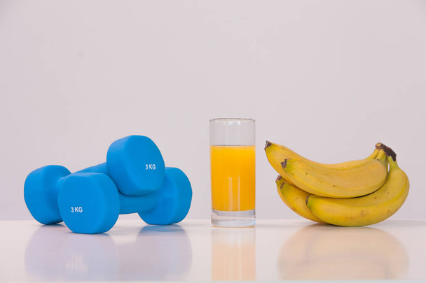 The concept of a healthy diet. Small dumbbells. Orange juice. Bananas. on a white background. healthy lifestyle. sport. Fitness food - Foto, immagini