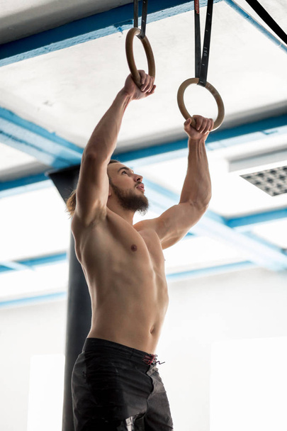 Muscle-up exercise athletic man doing intense workout at gym on gymnastic rings - 写真・画像
