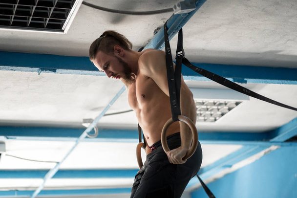 Muscle-up exercise athletic man doing intense workout at gym on gymnastic rings - Φωτογραφία, εικόνα
