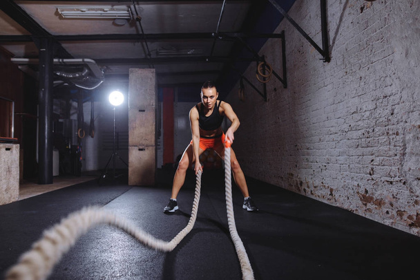 Young woman working out with battle ropes in cross fit gym - Foto, Bild