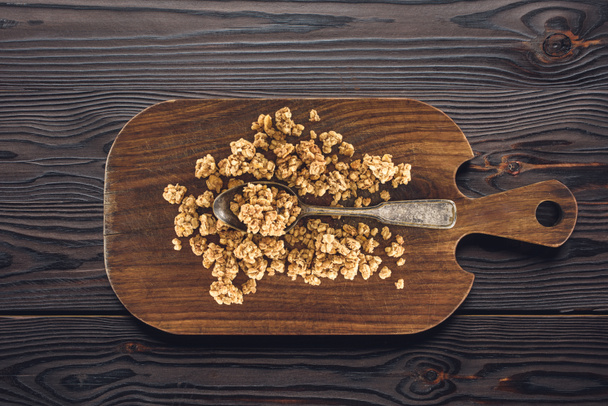 top view of crunchy granola and spoon on wooden board on table - Photo, Image