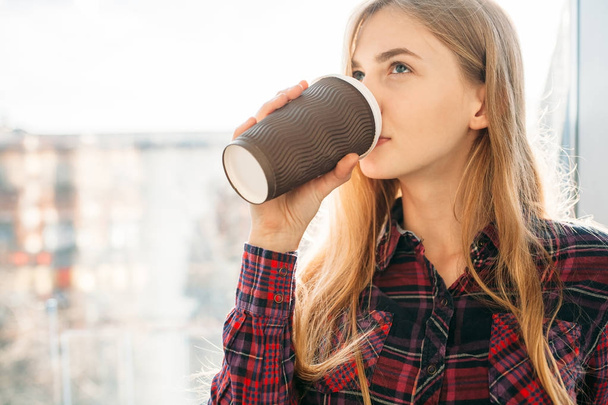 young beautiful girl drinking coffee, a woman in an office building, the bright sun - Фото, зображення