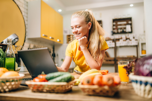 giovane donna felice cucina con computer portatile, cibo sano. Dieta vegetariana, verdure fresche e frutta
 - Foto, immagini