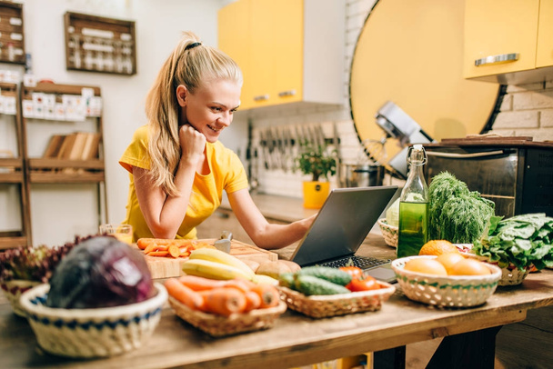 jovem mulher feliz cozinhar com laptop, comida saudável. Dieta vegetariana, legumes frescos e frutas
 - Foto, Imagem