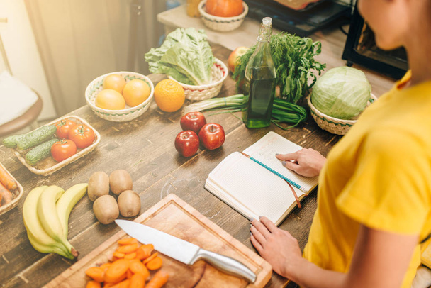 Mujer joven cocinando en la cocina, comida saludable. Dieta vegetariana, verduras y frutas frescas, libro de recetas sobre la mesa
  - Foto, Imagen