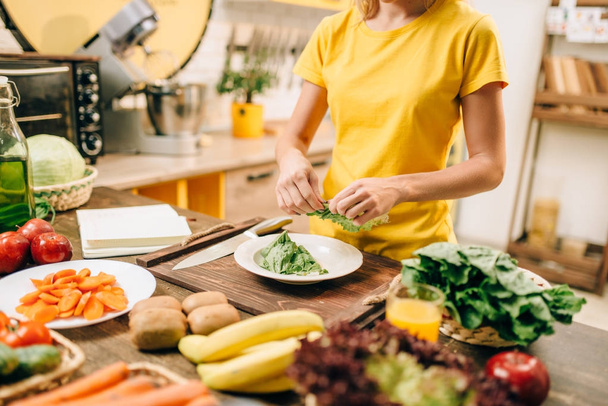 young woman holding lettuce in kitchen, cooking healthy food. Vegetarian diet, fresh vegetables and fruits on wooden table - Photo, Image