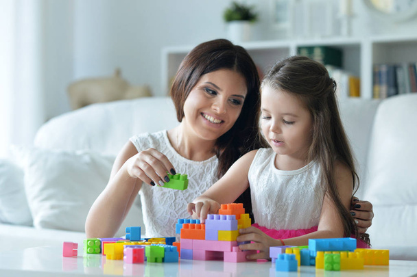 Кучерява маленька дівчинка і її мати грають з барвистими пластиковими блоками
 - Фото, зображення