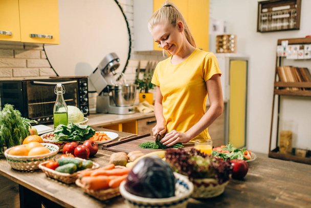 mujer feliz corte de eneldo en la mesa de madera, cocinar alimentos orgánicos. Dieta vegetariana, estilo de vida saludable
 - Foto, Imagen