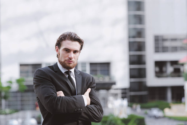 Confident young business man in black tie portrait. Handsome white male in black suit and tie, ginger hair and beard taken outdoor with natural light, confident business man concept. - 写真・画像