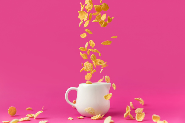close-up view of crispy corn flakes falling into milk jug on pink - Foto, imagen