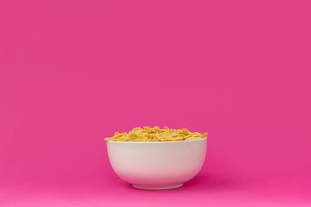 close-up view of white bowl with healthy tasty crunchy corn flakes isolated on pink - Фото, изображение