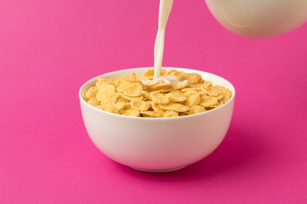 close-up view of milk pouring into bowl with corn flakes isolated on pink - Foto, imagen