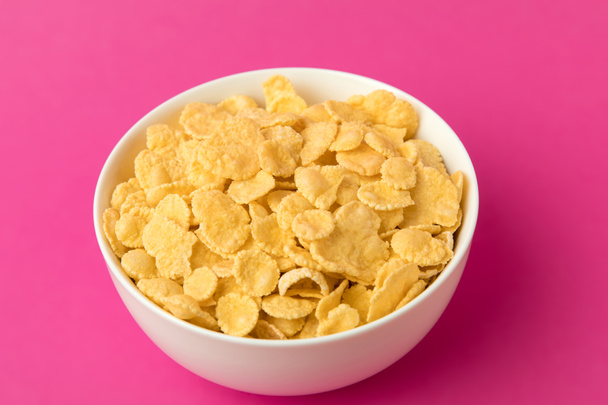 vista de cerca de un tazón blanco con hojuelas de maíz dulces y saludables aisladas en rosa
  - Foto, Imagen