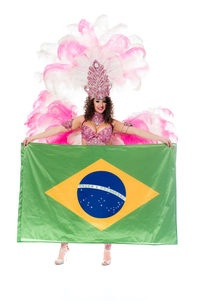 fröhliche junge Frau im Karnevalskostüm mit rosafarbenen Federn hält große Brasilien-Fahne auf weißem Grund - Foto, Bild