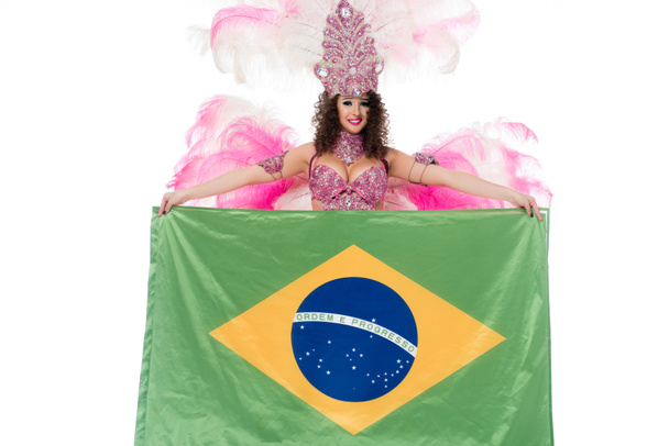 Bright woman in carnival costume with pink feathers holds large flag of Brasil isolated on white - Zdjęcie, obraz