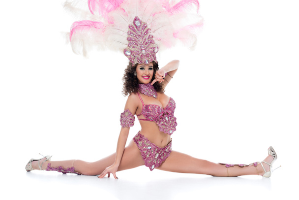 Heureuse jeune femme en costume de carnaval avec des plumes roses effectue split isolé sur blanc
 - Photo, image