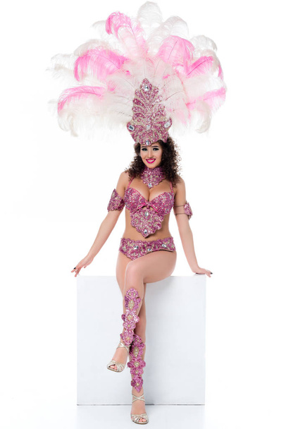 Bright woman in carnival costume with pink feathers sitting and posing seductively isolated on white - Photo, Image