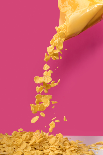 close-up view of corn flakes pouring out from bag on pink - Fotó, kép