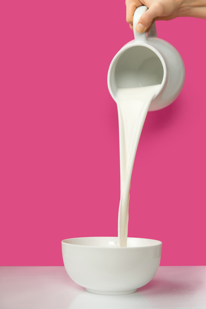 cropped shot of hand pouring fresh organic milk from jug to bowl on pink      - Photo, Image