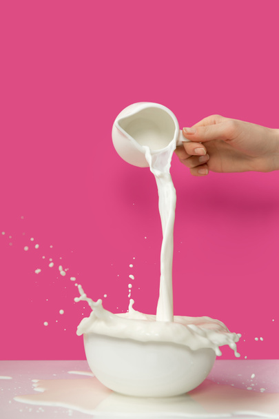bijgesneden schot van persoon verse gezonde melk van lokale kruik gieten kom op roze  - Foto, afbeelding