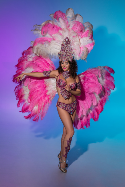 Bright woman in carnival costume with pink feathers performing on blue background - Foto, immagini