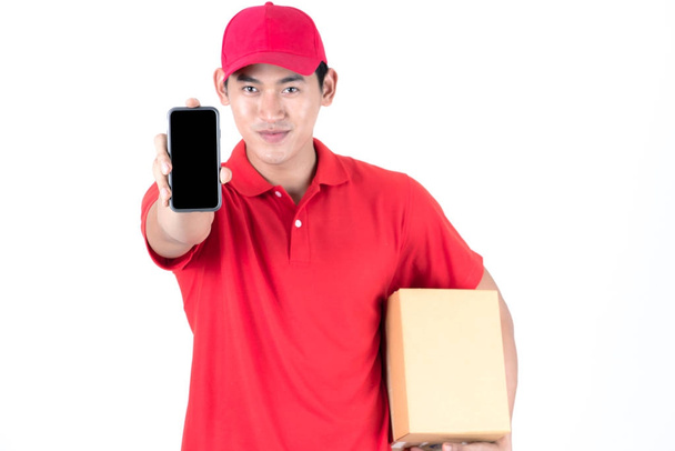 Koncepcja logistyczna kariery. Trzymając telefon w przód szczęśliwy dostawy. Na białym tle na białym tle. Azjatycki chiński pasuje mężczyzna w czerwonej koszulce polo i dżinsy z red hat w jego wczesnych lat dwudziestych. - Zdjęcie, obraz