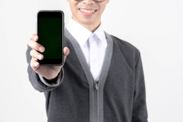 Confident young business man in smart grey sweater. Handsome asian male worker in grey sweater with black hair and glasses holding phone isolated in white background. - Zdjęcie, obraz